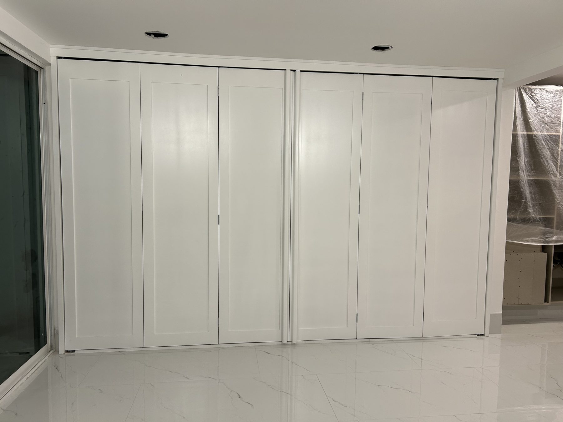 Clóset con puertas plegables blancas estilo shaker sobre piso de mármol