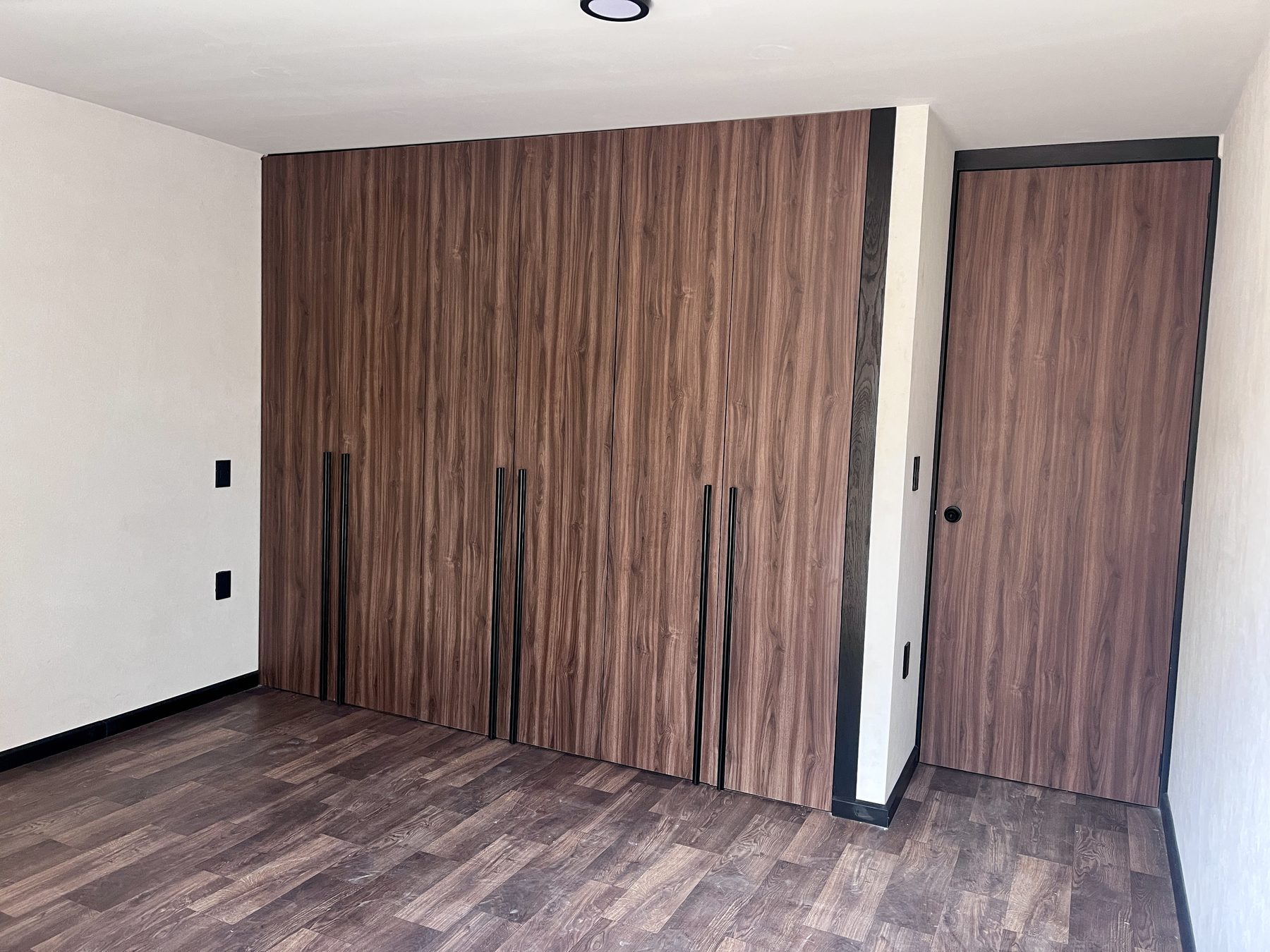 Clóset de piso a techo en tono nogal con jaladeras negras largas y puerta a juego