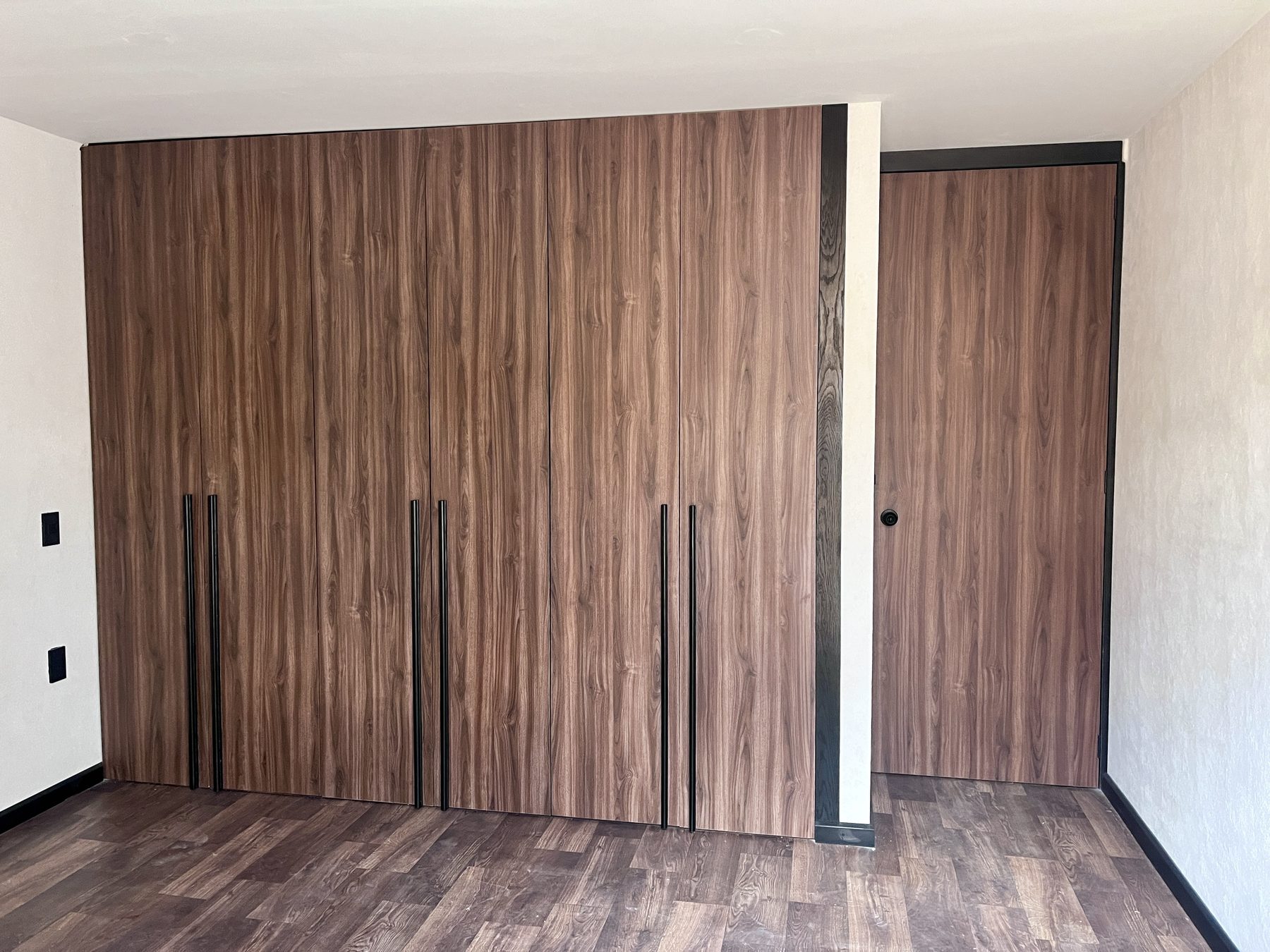 Clóset de piso a techo en tono nogal con jaladeras negras largas y puerta a juego